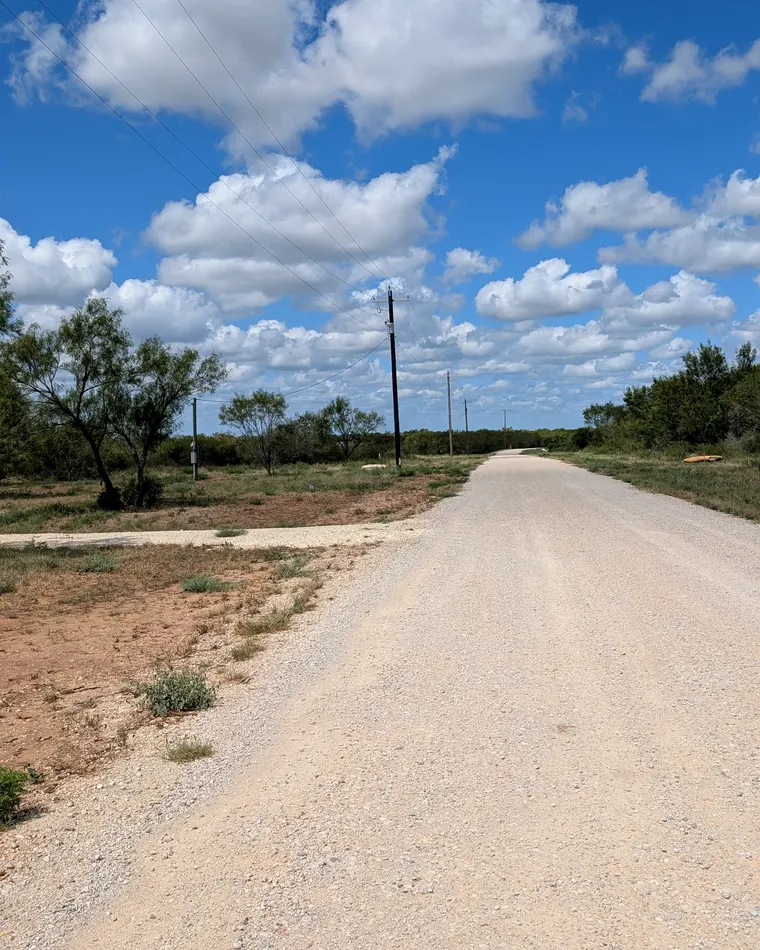 Caliche road with power poles under big white clouds