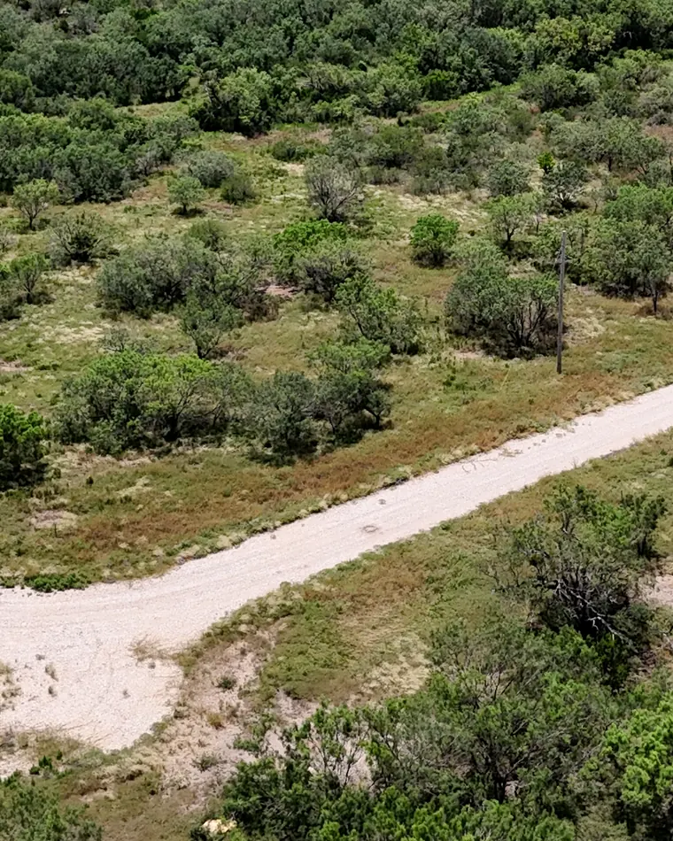 Aerial view of two caliche roads meeting between green lots, with a pole line