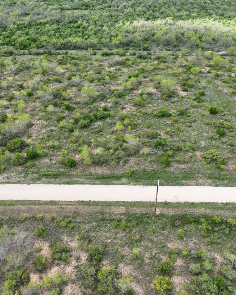 Top-down aerial of a green brush lot along a caliche road with a power pole